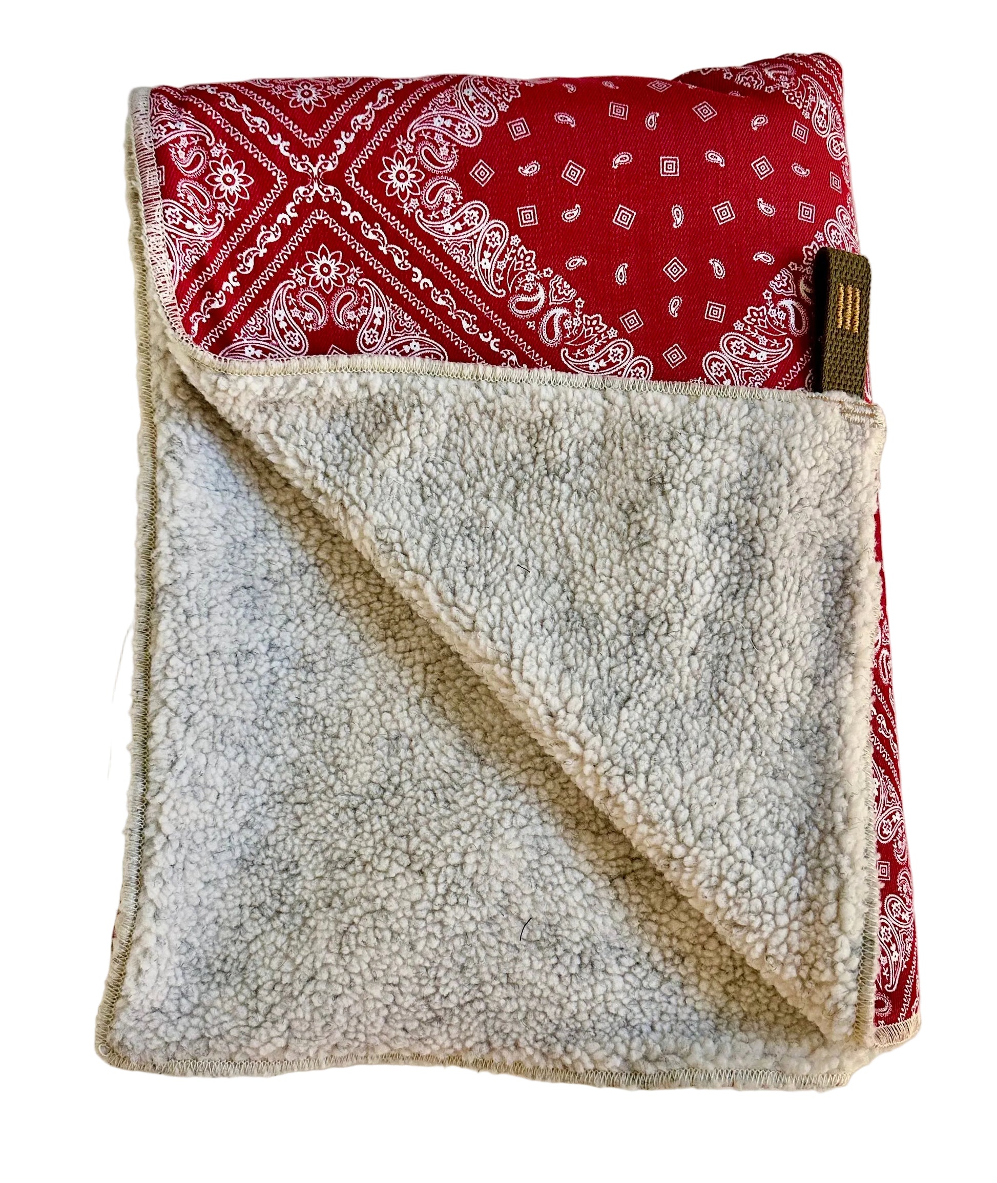 Folded blanket with red bandana pattern on one side and gray fleece on the other, on a light background.